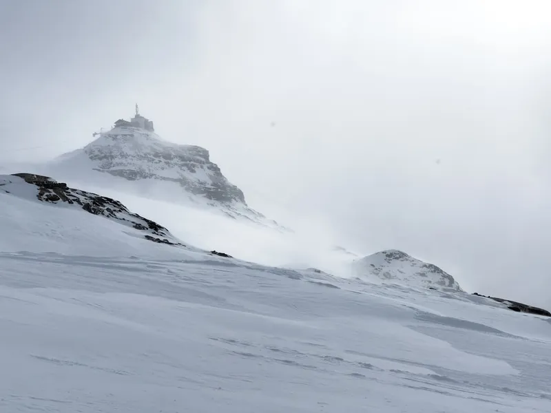 Snowy mountain landscape with mist rising from peaks and a remote refuge on a mountaintop